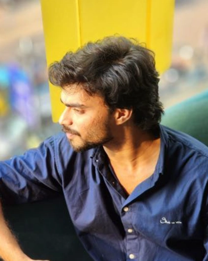 Portrait of a young man in a blue shirt sitting and looking away with natural light.
